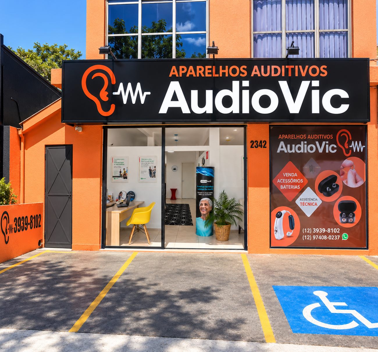 Fachada da AudioVic Aparelhos Auditivos na Avenida Andrômeda, 2342, com prédio laranja, placa preta e vitrine adesivada