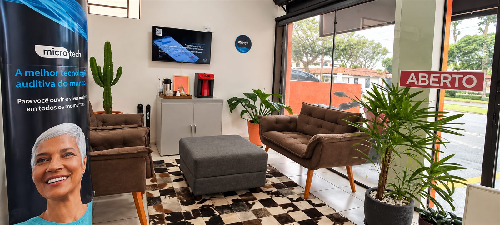 Recepção da AudioVic com poltronas, mesa com café, televisão na parede e totem da marca microTech